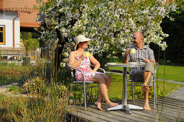 Paar beim Kaffeetrinken am Gartenteich vor blühendem Kirschbaum