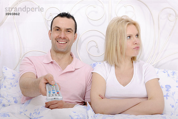 Mann und Frau im Bett  Streit um das Fernsehprogramm  Mann mit Fernbedienung  Frau unzufrieden und beleidigt