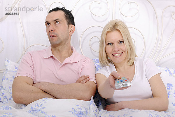 Mann und Frau im Bett  Streit um das Fernsehprogramm  Frau mit Fernbedienung  Mann unzufrieden und genervt