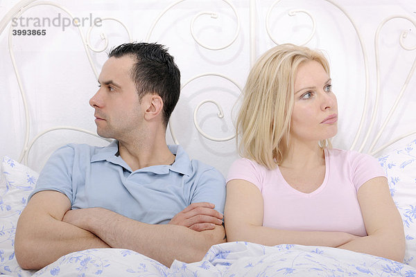 Paar im Bett hat Streit  Mann und Frau mit verschränkten Armen blicken in unterschiedliche Richtungen  wütend und verletzt