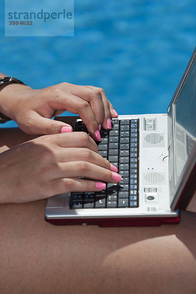 Junge Frau mit Computer am Pool