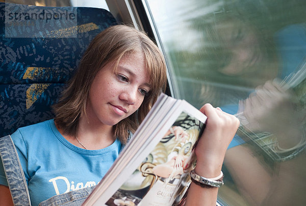 Mädchen sitzt alleine in einem in einem Zug und liest eine Zeitschrift  Deutschland