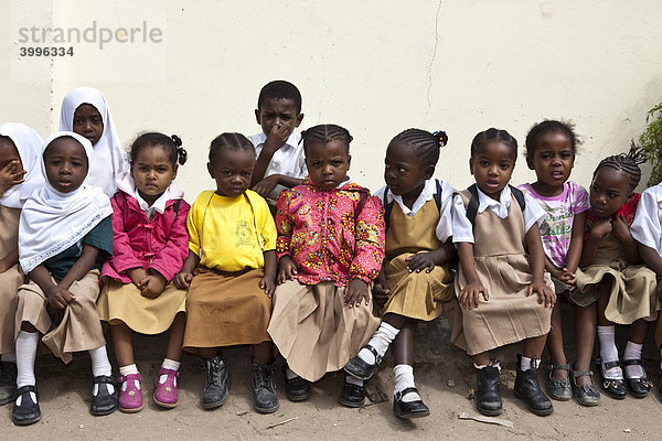 Schulkinder sitzen an einer Mauer zu den Feierlichkeiten zum Parents Day in der Ortschaft Mwanakwerekwe  Sansibar  Tansania  Afrika