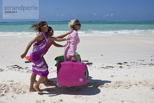 Mutter mit zwei Kindern trägt die schweren Koffer am Strand