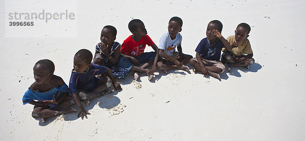 Kinder sitzen in einer Reihe am Strand  Sansibar  Tansania  Afrika