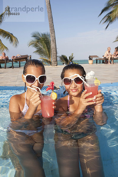 Zwei Mädchen mit Sonnenbrillen  ca 12 Jahre  trinken in einem Swimmingpool Cocktails