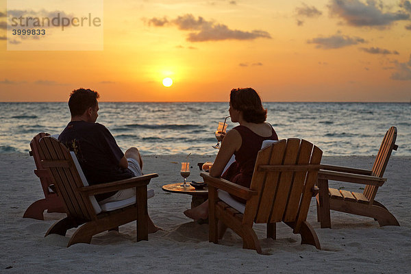 Paar auf Stühlen am Strand mit Longdrink vor untergehender Sonne  Meer  Rihiveli  Insel  Malediven  Süd Male Atoll  Archipel  Indischer Ozean  Asien