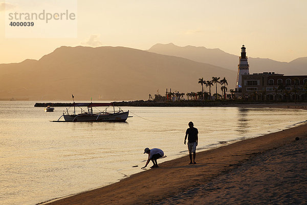 Menschen spazieren am Abend am Strand  Leuchtturm  Berge  Boot  Banka  Abend  stimmungsvoll  Olongapo City  Subic Bay  Insel Luzon  Philippinen  Südchinesisches Meer  Pazifik