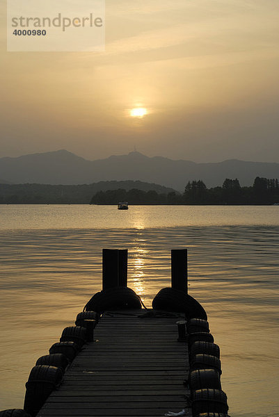 Abendsonne mit hölzerner Steg am Westsee  chinesisch: Xi Hu  vor Bergkulisse und Ausflugsboot  Hangzhou  China  Asien