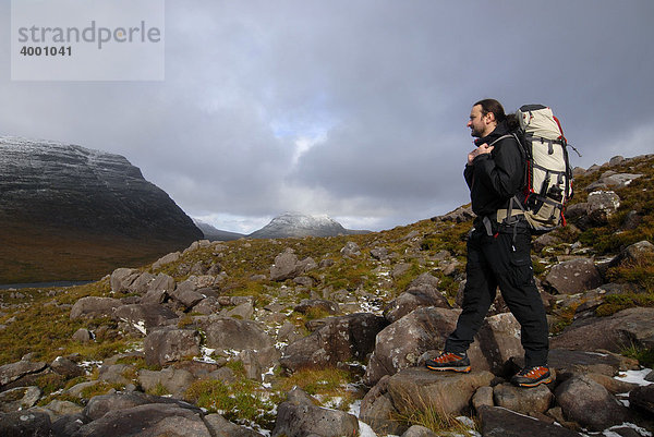 Wanderer mit Trekkingrucksack auf Bergtrekkingpfad vor verschneitem Gipfel  Liathach  Torridon  Schottland  Großbritannien  Europa