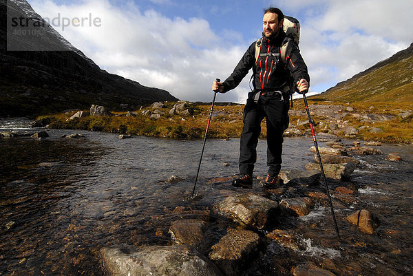 Wanderer mit Trekkingrucksack und Teleskopstöcken überquert Gebirgsfluss  Liathach  Torridon  Schottland  Großbritannien  Europa