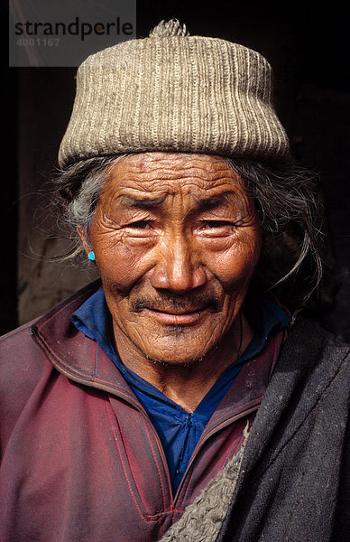 Tibetischer Nomade  tibetischer Mann mit grauen Haaren in einfacher Nomadenkleidung mit Wollmütze und Türkisohrring  Portrait  Tibet  China  Asien