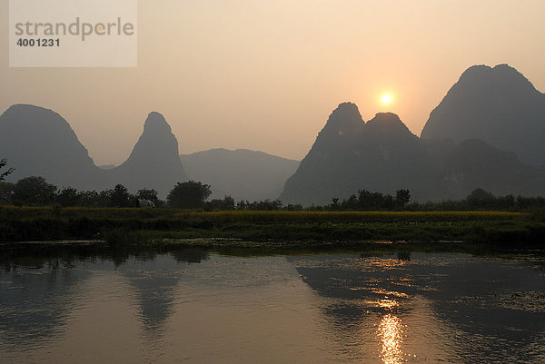 Karstfelsen und Reisfelder zur Erntezeit spiegeln sich in der Abendsonne im Yulong Fluss in der Karstfelsenlandschaft bei Yangshuo  Guilin  Guangxi  China  Asien