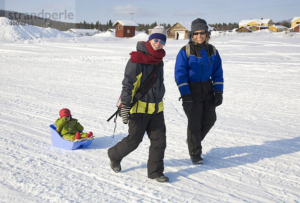 Zwei Frauen mit einem einjährigen Mädchen in einem Schlitten wandern auf dem zugefrorenen Fluss Torne Aelv am Rande der Ortschaft Jukkasjärvi in Lappland  Nord-Schweden  Schweden