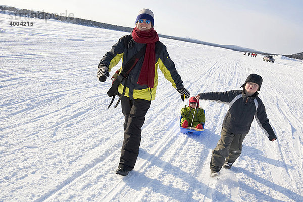 Eine Frau und zwei Mädchen in einem Schlitten auf dem zugefrorenen Fluss Torne Aelv am Rande der Ortschaft Jukkasjärvi in Lappland  Nord-Schweden  Schweden
