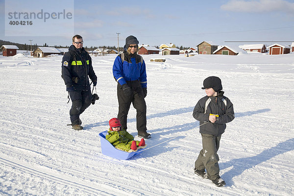 Ein Mann und eine Frau in den Vierzigern mit zwei Kindern wandern auf dem zugefrorenen Fluss Torne Aelv am Rande der Ortschaft Jukkasjärvi in Lappland  Nord-Schweden  Schweden