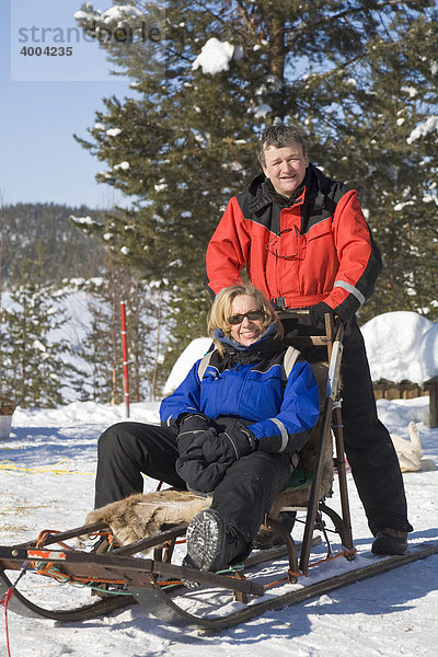 Eine Frau und ein Mann auf einem Schlitten bei einer Hundeschlitten-Fahrt in Kiruna  Lappland  Nord-Schweden  Schweden