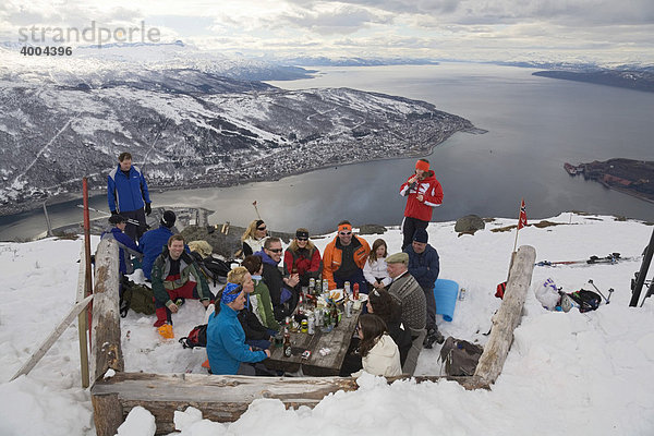 Eine Gruppe von Ausflüglern sitzt hoch über Narvik und dem Ofotfjorden am Berg Fagernes-Fjellet im Schnee  in Narvik  Norwegen