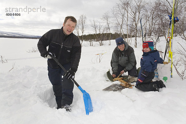 Vorbereitungen zur Grillparty in Lappland  ein Mann gräbt einen Graben in den Schnee  Frau und Kind machen Feuer in Kiruna  Lappland  Nord-Schweden  Schweden