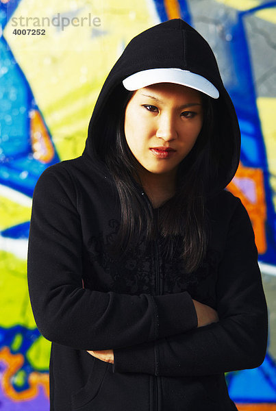 Junges asiatisches Mädchen im Rapperstil vor Graffiti Wand