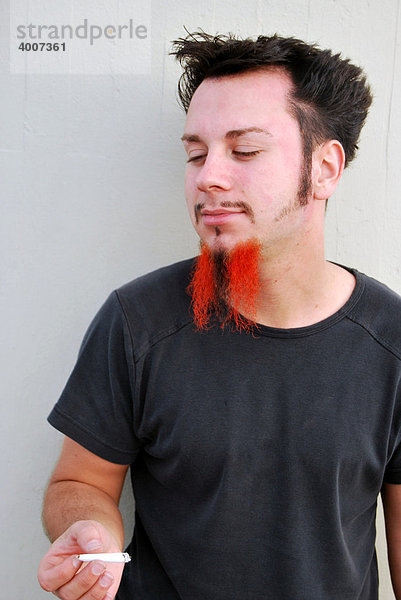 Drogen  junger Mann mit rot-schwarzem Bart hält einen Joint  selbstgedrehte Zigarette in der Hand