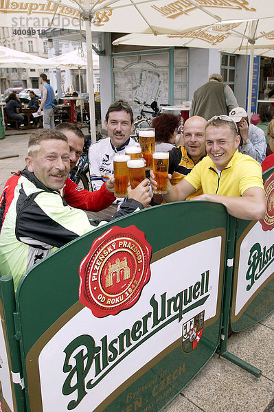 Radfahrer  Männer  stoßen in einem Biergarten auf dem Platz der Republik mit einem Bier an  Pilsner Urquell  in Pilsen  Plzen  Böhmen  Tschechien  Europa