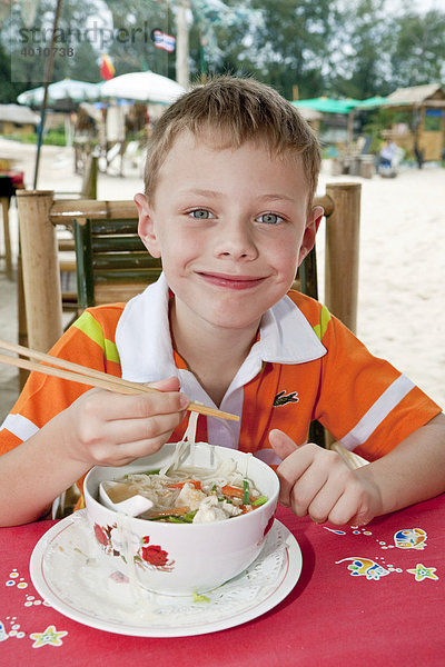 Ein Junge 6 Jahre isst eine Nudelsuppe mit Stäbchen Insel Phuket Südthailand Thailand Südostasien Asien