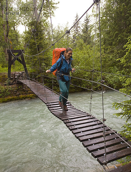 Wanderin mit Rucksack überquert eine Hängebrücke über den Taja Fluss in der Nähe der alten Stadt Canyon City  Pazifischer nordwestlicher Küstenregenwald  Chilkoot Trail  Chilkoot Pass  Alaska  USA