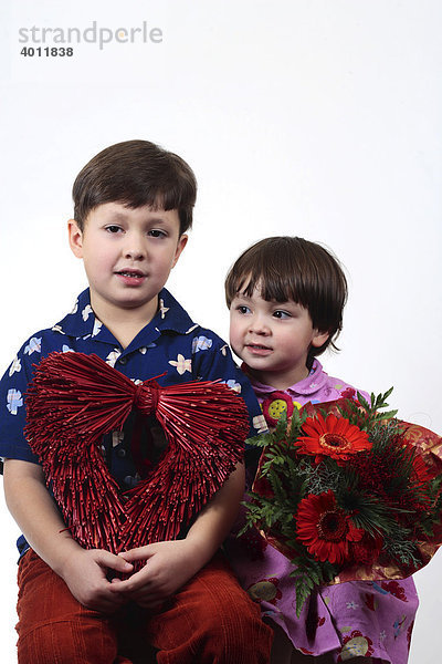 Sechsjähriger Junge und zweijähriges Mädchen mit Blumen und rotem Herz