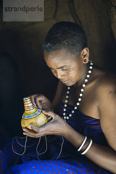 Eine Frau vom Stamm der Datooga dekoriert eine Kalebasse mit Glasperlen  Lake Eyassi  Tansania  Afrika