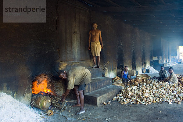 Kopra-Produktion  Arbeiter entfacht ein Feuer unter einer Halle in der Kokosnüsse getrocknet werden  rechts entfernen Arbeiter das trockene Kokosnussfleisch aus der Schale  Quelimane  Mosambik  Afrika
