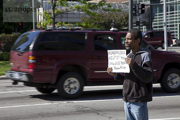 Ein Mann steht mitten auf einer belebten Straße und bettelt Fahrer um Geld für Lebensmittel an  Detroit  Michigan  USA
