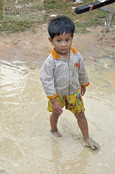 Kleiner Junge läuft durch eine Regenpfütze  Slums von Siem Reap  Kambodscha  Asien