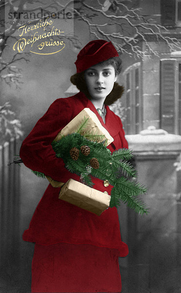 Historische Weihnachtskarte  junge Frau mit Geschenken und Tannengrün in rotem Kostüm mit Hut  Herzliche Weihnachtsgrüße