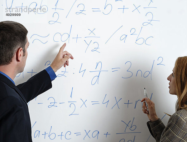 Ein Mann und eine Frau sehen sich Kalkulationen und Formeln auf einer Weißwandtafel an