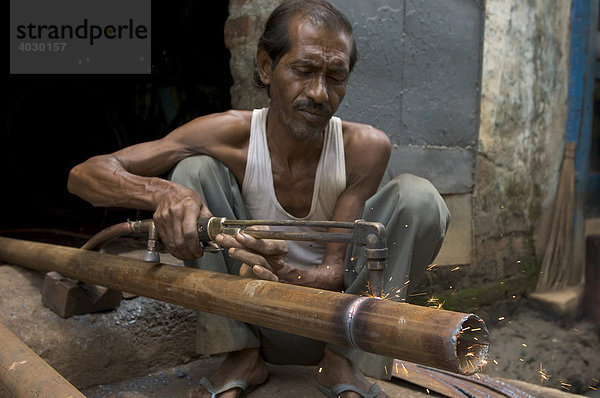 Indischer Stahlarbeiter. Für Arbeiten die in Europa von computergesteuerten Maschinen verrichtet werden braucht man hier nur einen Arbeiter mit ruhiger Hand und einen Schneidbrenner. Howrah  Hooghly  Westbengalen  Indien