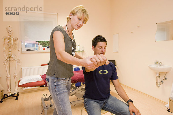 Physiotherapeutin  Lehrerin für Alexandertechnik führt mit einem Patienten eine Entspannungsübung zur Steigerung der Greiffähigkeit im Praxisraum durch