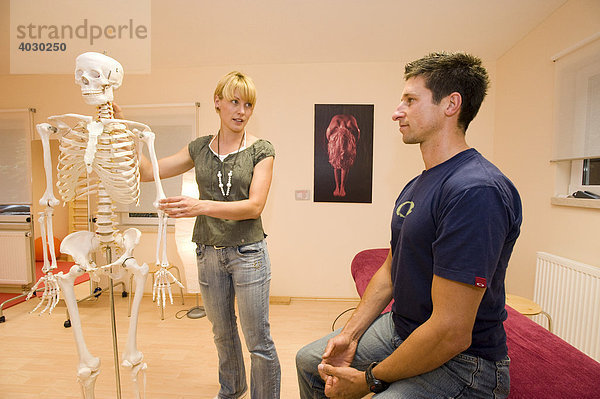 Physiotherapeutin  Lehrerin für Alexandertechnik gibt einem Patienten Erklärungen zu Anatomie mithilfe eines künstlichen Skeletts