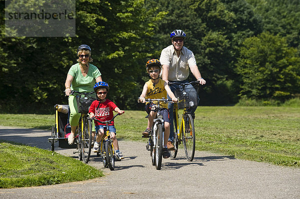 Familie mit 2 Kindern fährt mit Helmen auf Fahrrädern in Park