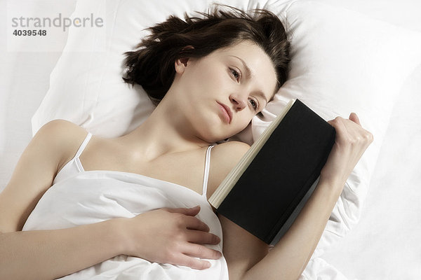 Junge brünette Frau liest ein Buch im Bett