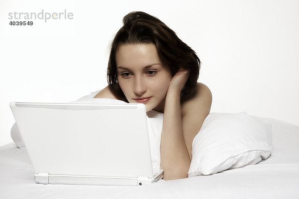 Junge brünette Frau arbeitet mit ihrem Laptop im Bett