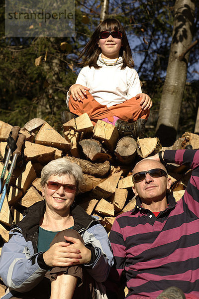 Großeltern mit Enkelin  vor Holzstoß