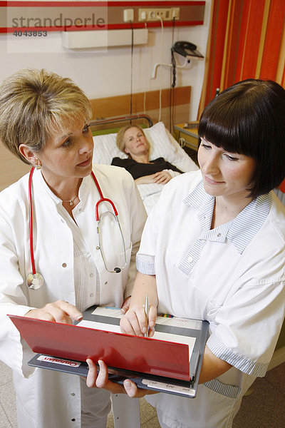 Ärztin und Krankenschwester besprechen sich bei einer Visite im Krankenzimmer einer Patientin in einem Krankenhaus