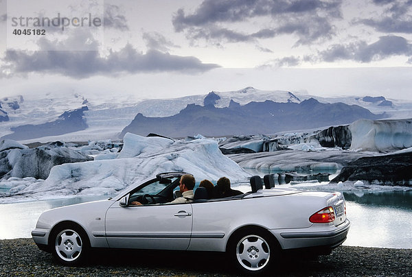 Pärchen sitzt in einem silbernen Mercedes Cabriolet mit offenem Verdeck vor einem Gletschersee  Jökulsárlón am Fuße des Vatnajökull  Island  Europa