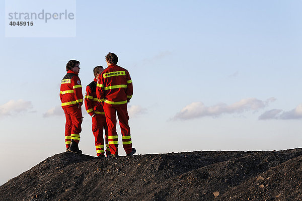 Drei junge Männer in oranger Rettungsdienst-Einsatzkleidung stehen auf Schutthalde  Halde Hoheward  Herten  Recklinghausen  Ruhrgebiet  Nordrhein-Westfalen  Deutschland  Europa