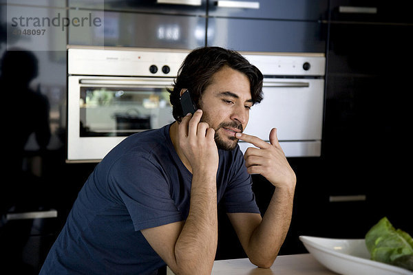 Mann telefoniert in der Küche mit Handy