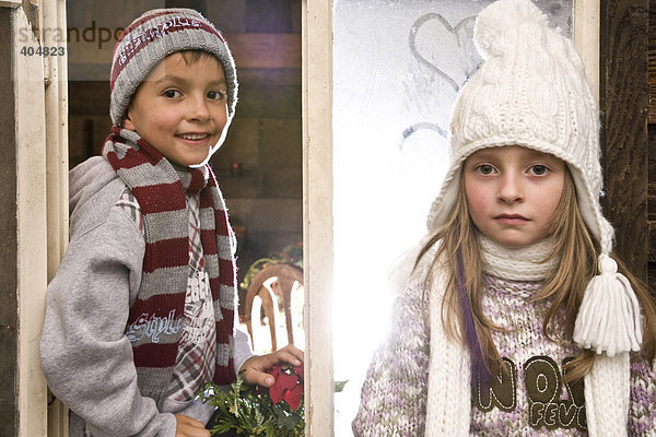 Zwei Geschwister-Kinder spielen am Fenster einer Wanderhütte