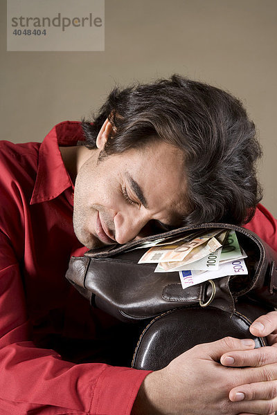 Junger Mann ruht sich zufrieden auf seiner gefüllten Geldtasche aus