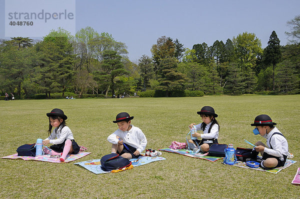 Schüler in Schuluniform und Namensschild einer Eliteschule bei der Mittagspause essen mit Stäbchen im Botanischen Garten in Kyoto  Japan  Asien