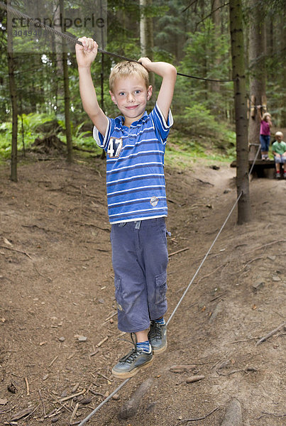 Ein Junge  6 Jahre  balanciert auf einem Kletterseil im Wald